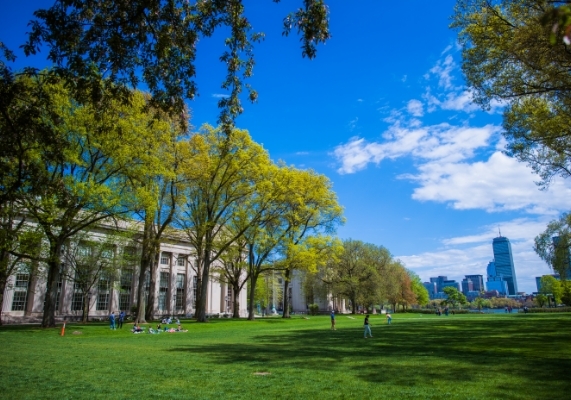 The grassy lawn of Killian Court, with campus buildings and trees on one side and the Boston skyline visible in the distance.