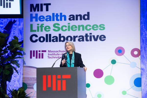 President Kornbluth stands behind a podium on stage and speaks at MIT HEALS.