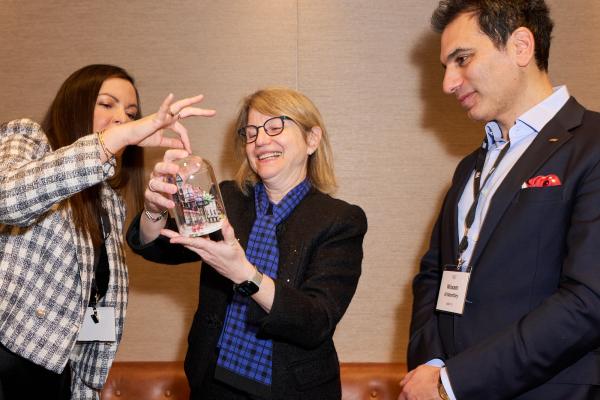 President Kornbluth holds a gift and stands in the center of two MIT Alumni Association members in London.